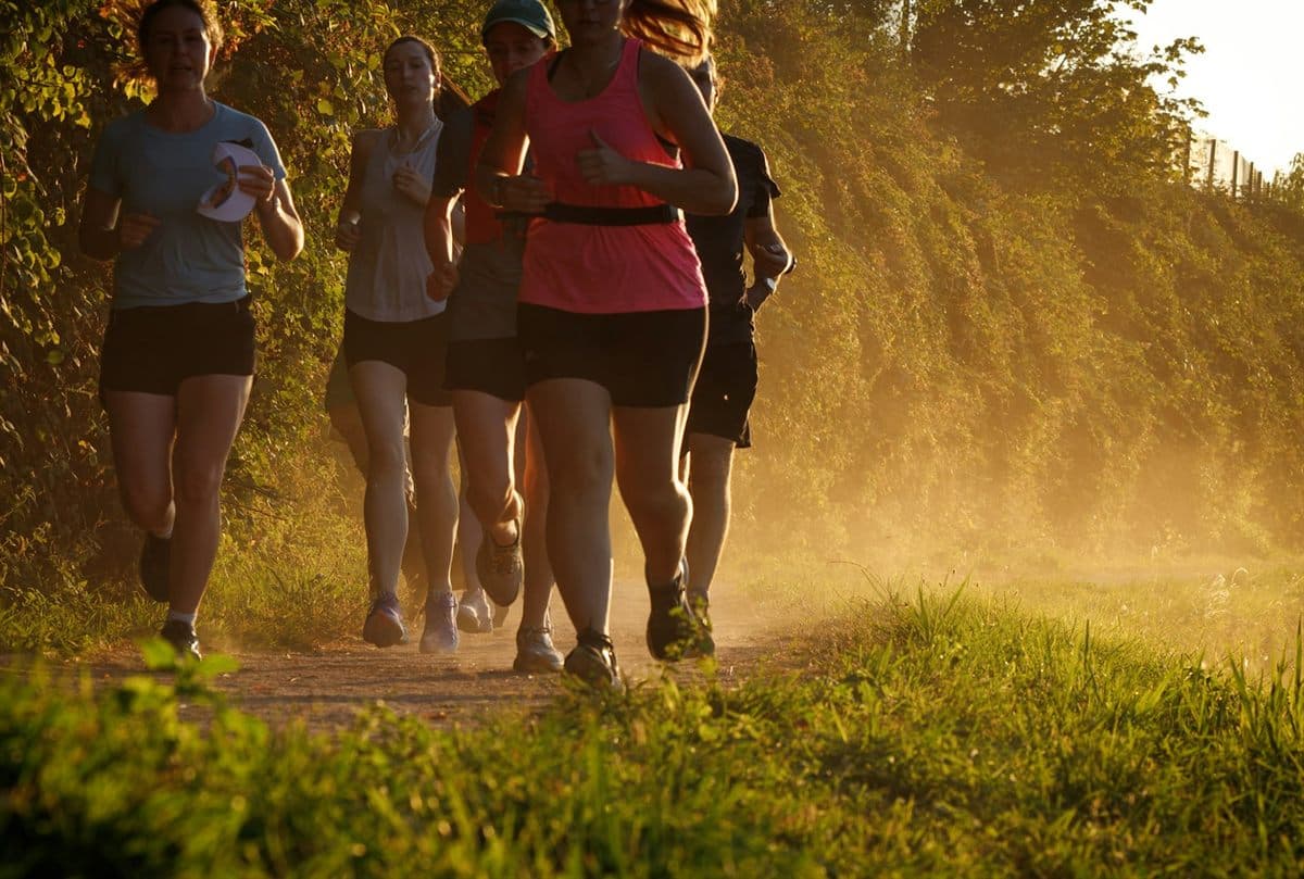 A group of women running together on a trail at sunset